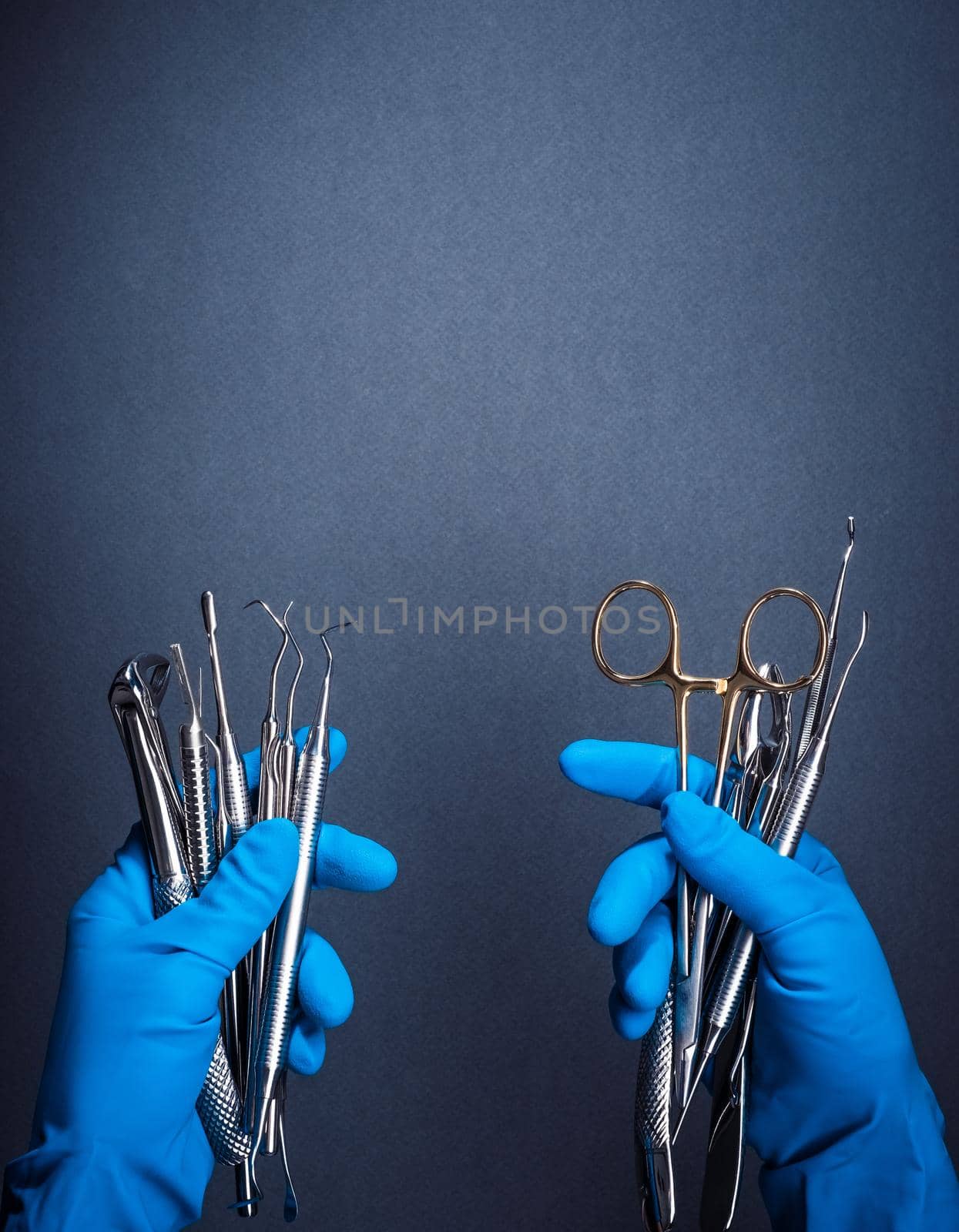Hands in blue gloves holding metal dental equipment on gray background with copy space