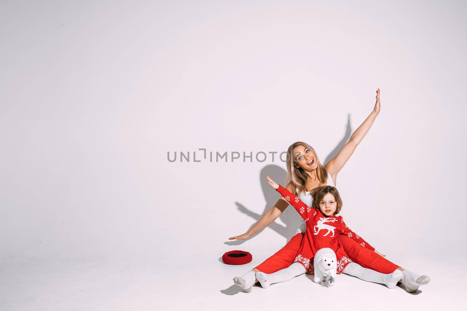 Christmas concept photo of excited young lady and little girl sitting on floor and spreading their arms. Copy space