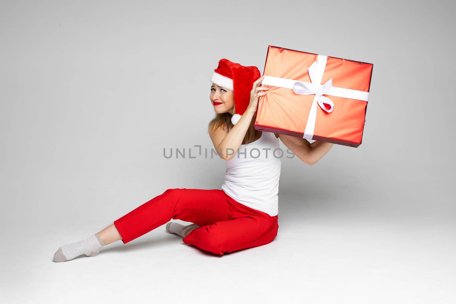 Worried beautiful lady wearing Santa hat with big gift box by StudioLucky