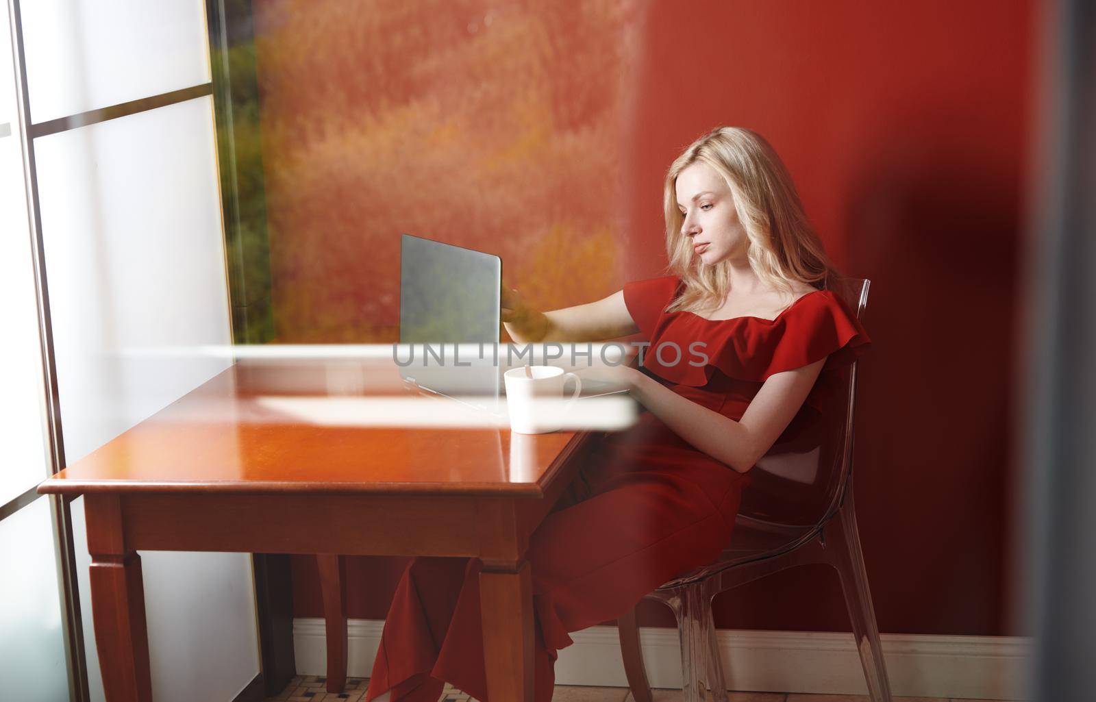 Young adult woman sitting at the table and working on laptop