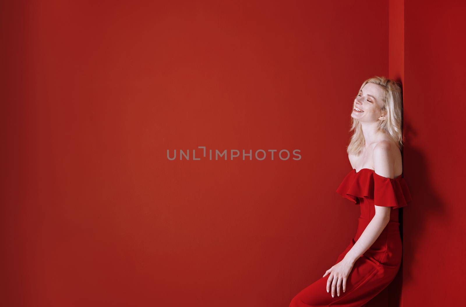 Beautiful young adult woman wearing red jumpsuit standing next to the wall