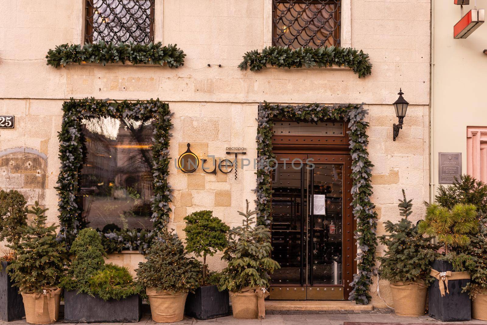 Christmas street decor. Stylish christmas wreath with baubles, empty board with copy space on rustic wooden door at holiday market in city street. Space for text.