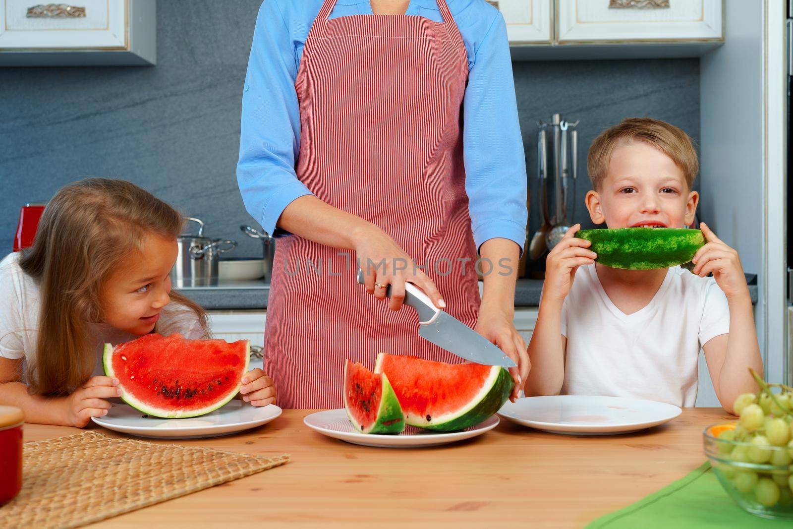 Sweet family, mother and her kids eating watermelon in their kitchen having fun by Fabrikasimf