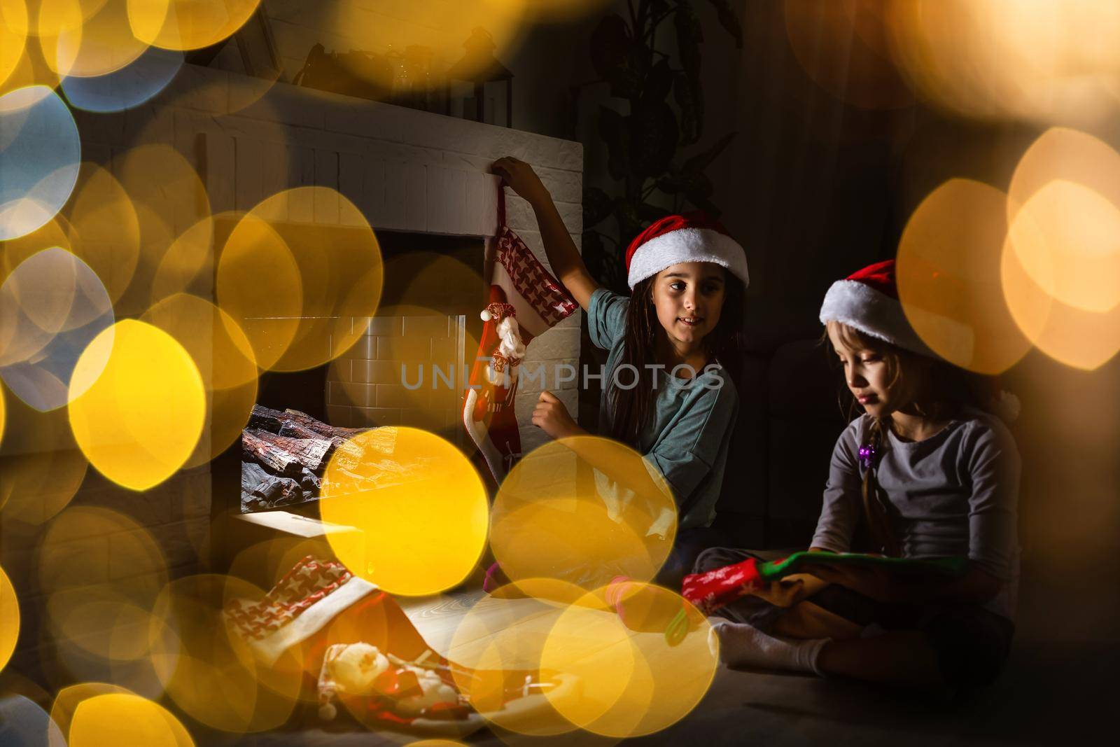 Little kids opening presents next to the fireplace in a cozy home celebrating Christmas