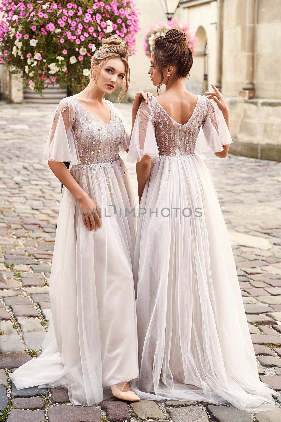 Beautiful bridesmaids in gorgeous light silver dresses in old beautiful European city on a wedding day in summer. Dresses are floor length or full-lenghth long tulle with half sheer sleeves and side slit.