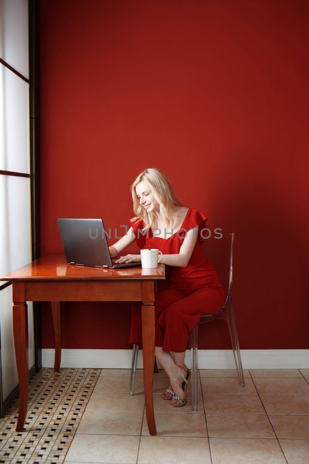 Young adult woman sitting at the table and working on laptop