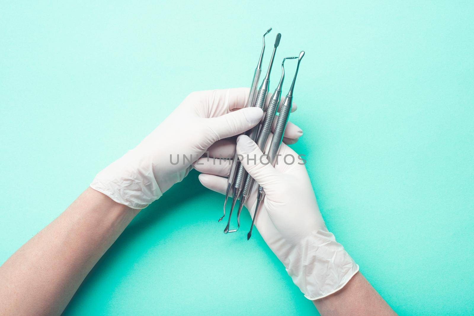 Hands in glove with dental tools on light turquoise background