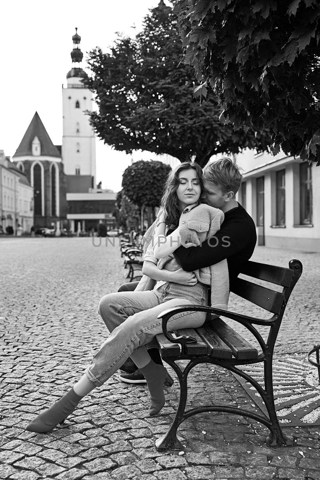 Beautiful young couple cuddling on a bench in a European town. Romatnic date and love concept. by berezko