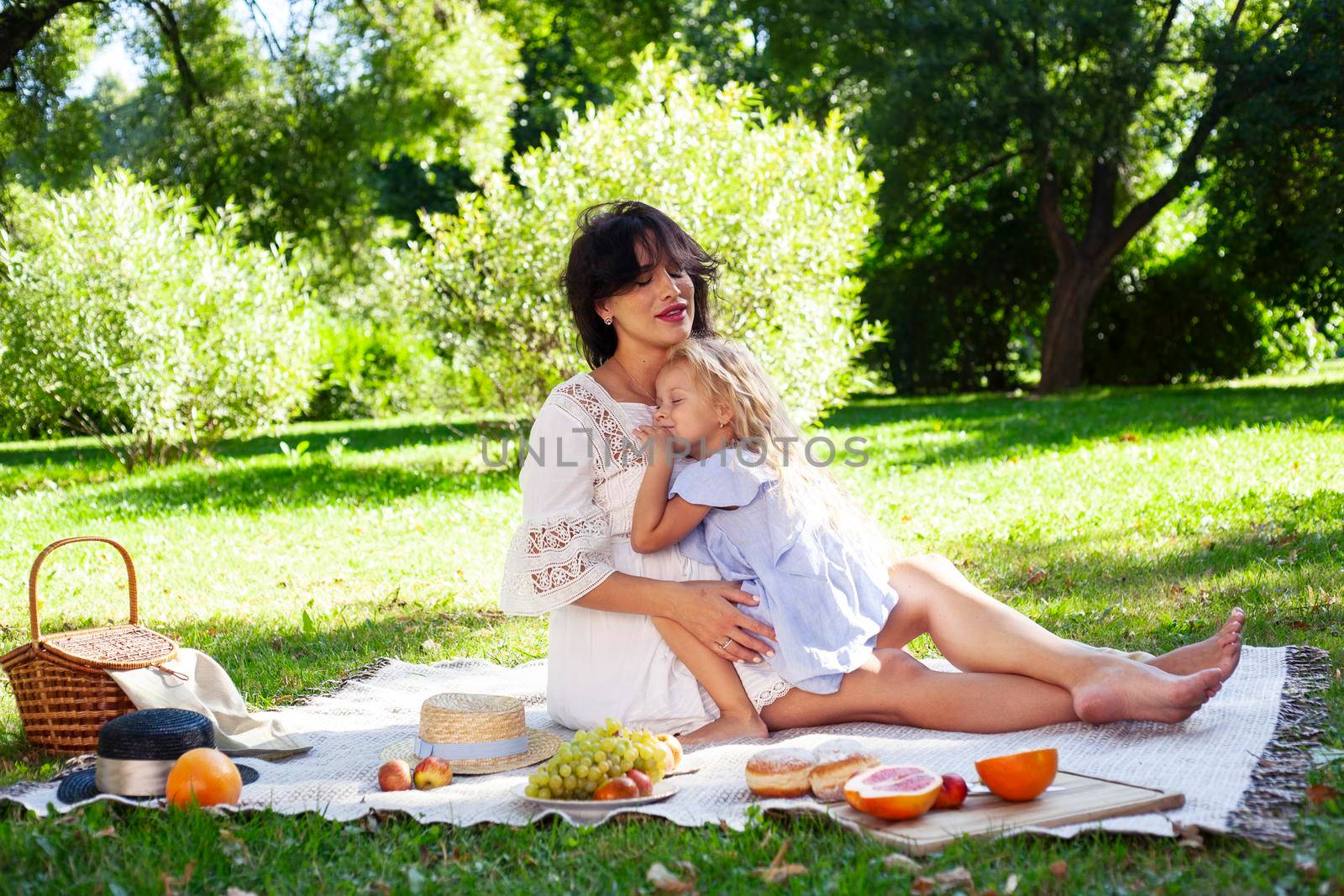 young pretty pregnant brunette woman having fun with her daughter on picnic on green grass in park, lifestyle people concept close up