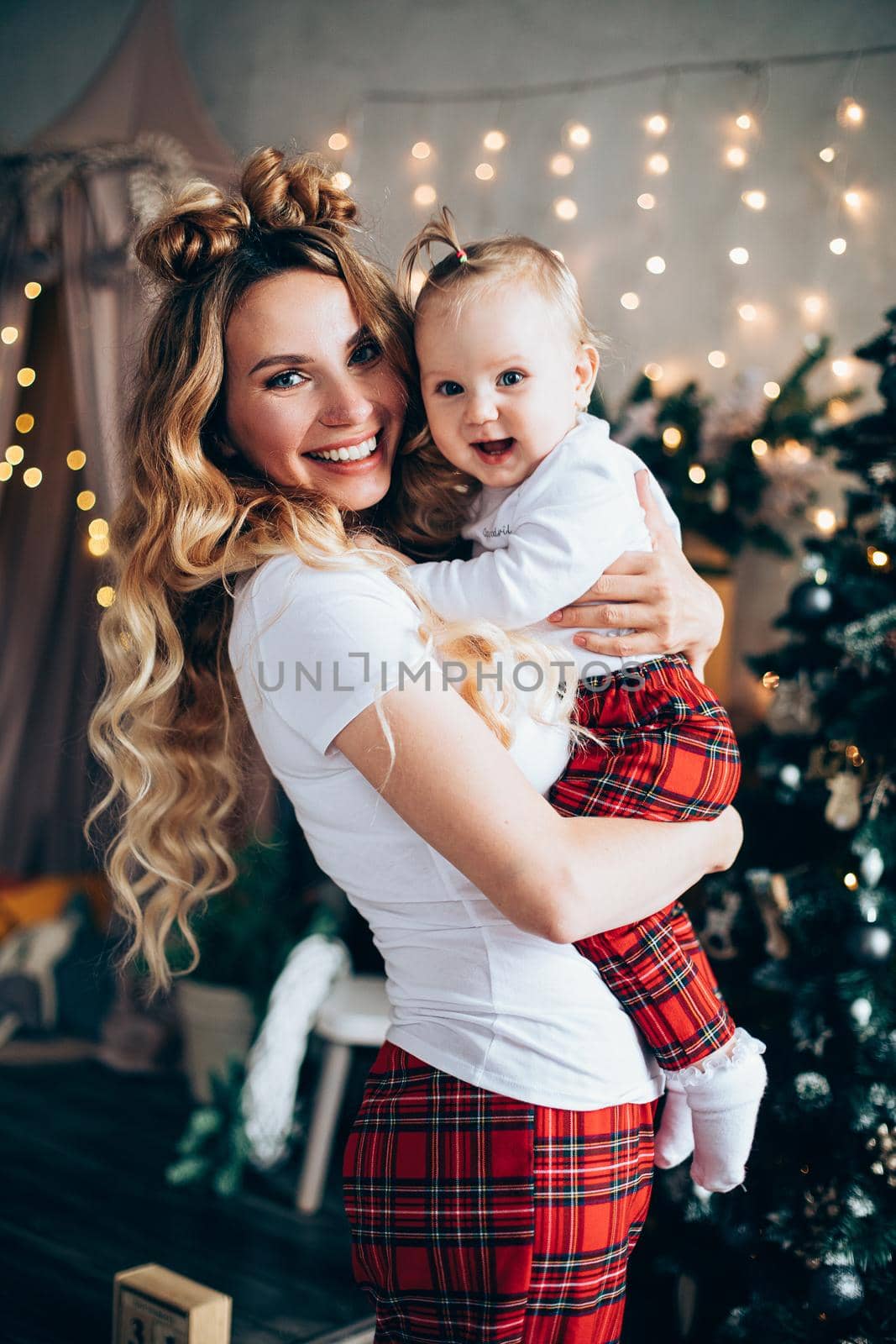 Handsome young mum holds her baby near the christmas tree by StudioLucky