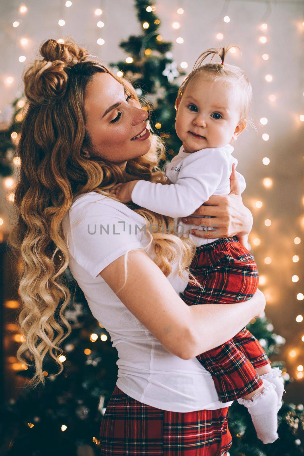 Attractive young mum hold a baby on her knees in christmas atmosphere by StudioLucky