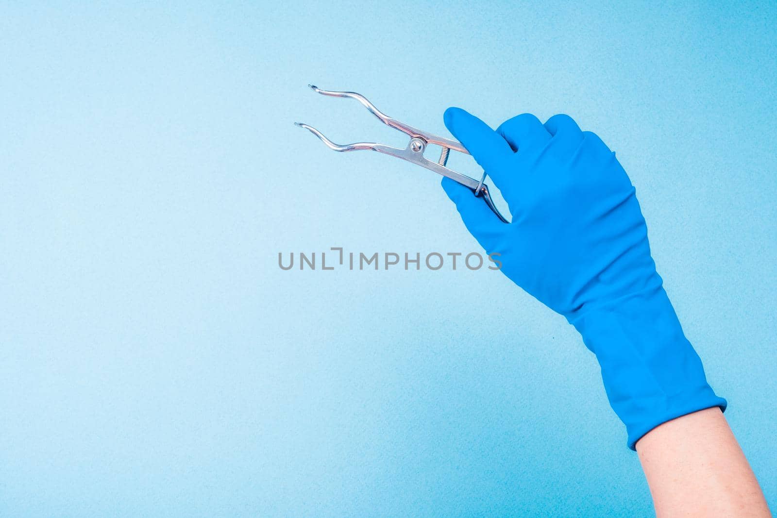 Hand in blue glove holding dental metal clamps on light blue background