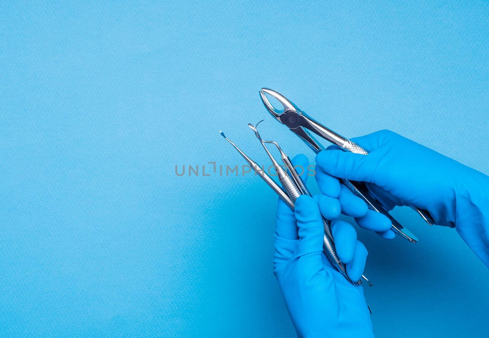 Hands in blue gloves holding dental clamps and surgery sticks on light blue background