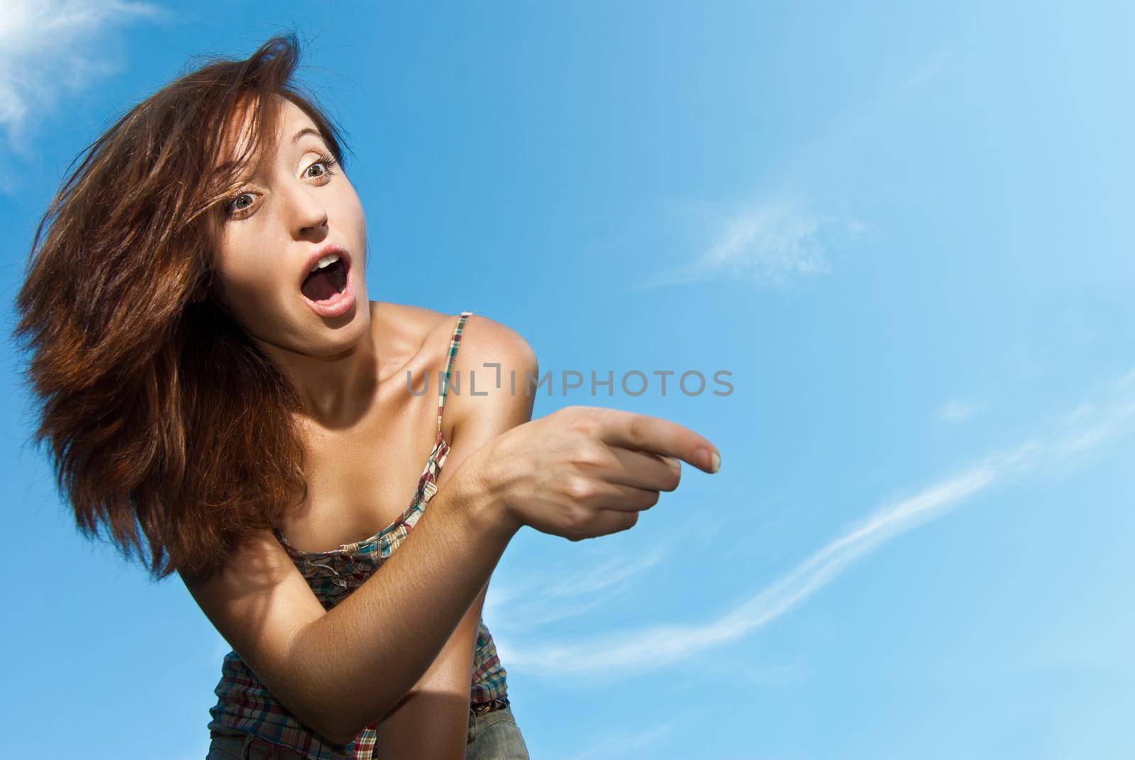 Portrait of a beautiful young woman amazed and pointing against the sky - Outdoor
