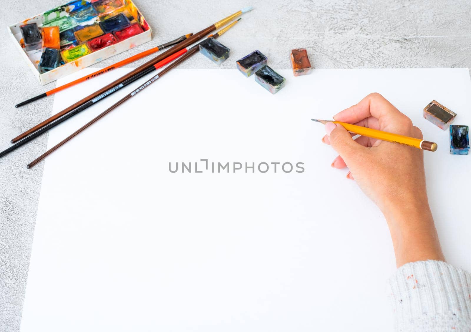 Top view of girl's hand drawing with pencils and paints