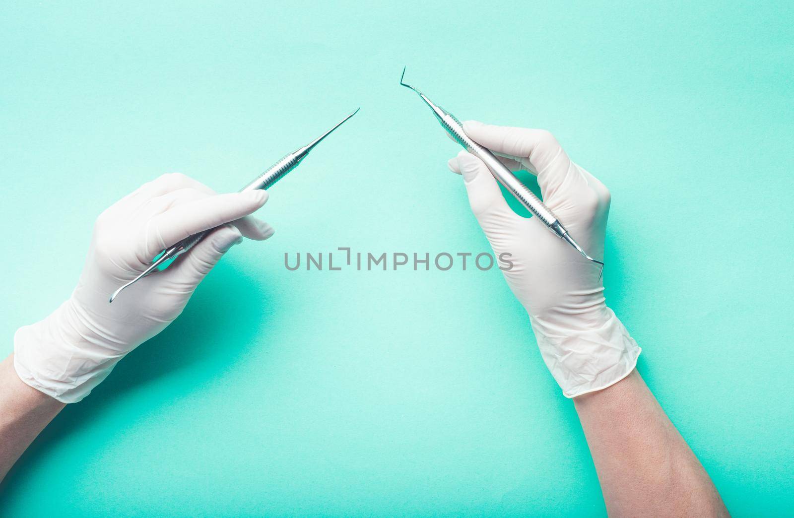 Top view of hands holding dental tools on light turquoise background