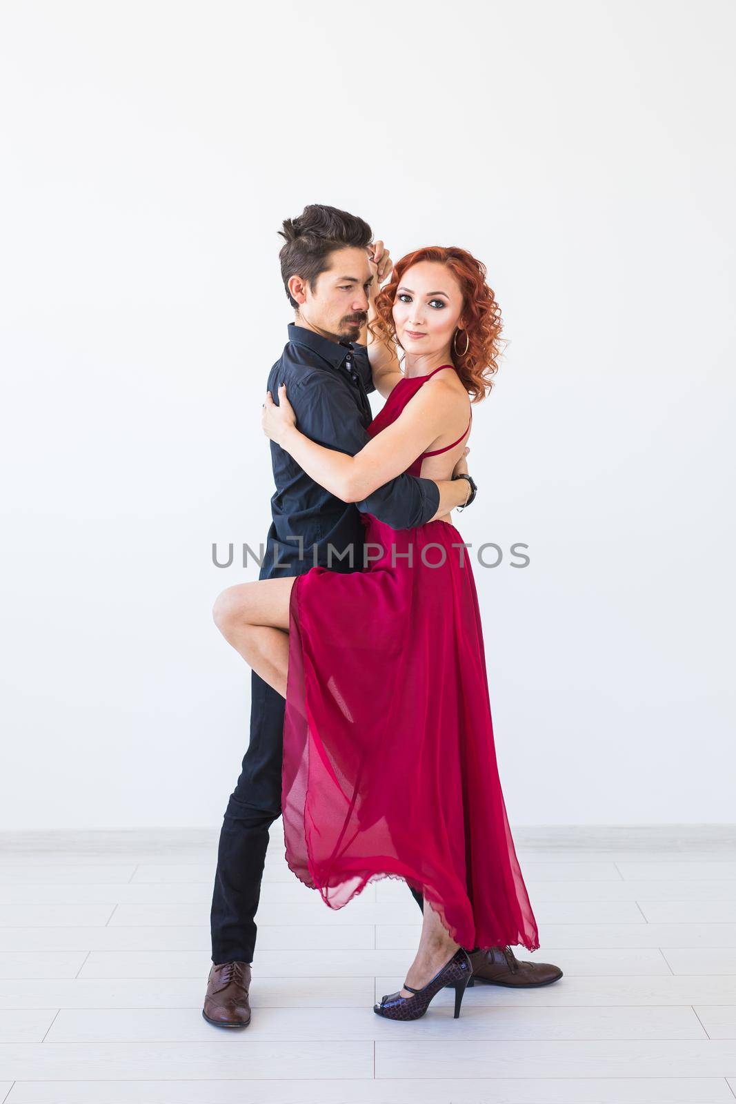 Social dance, bachata, kizomba, salsa, tango concept - Woman dressed in red dress and man in a black costume over white background.