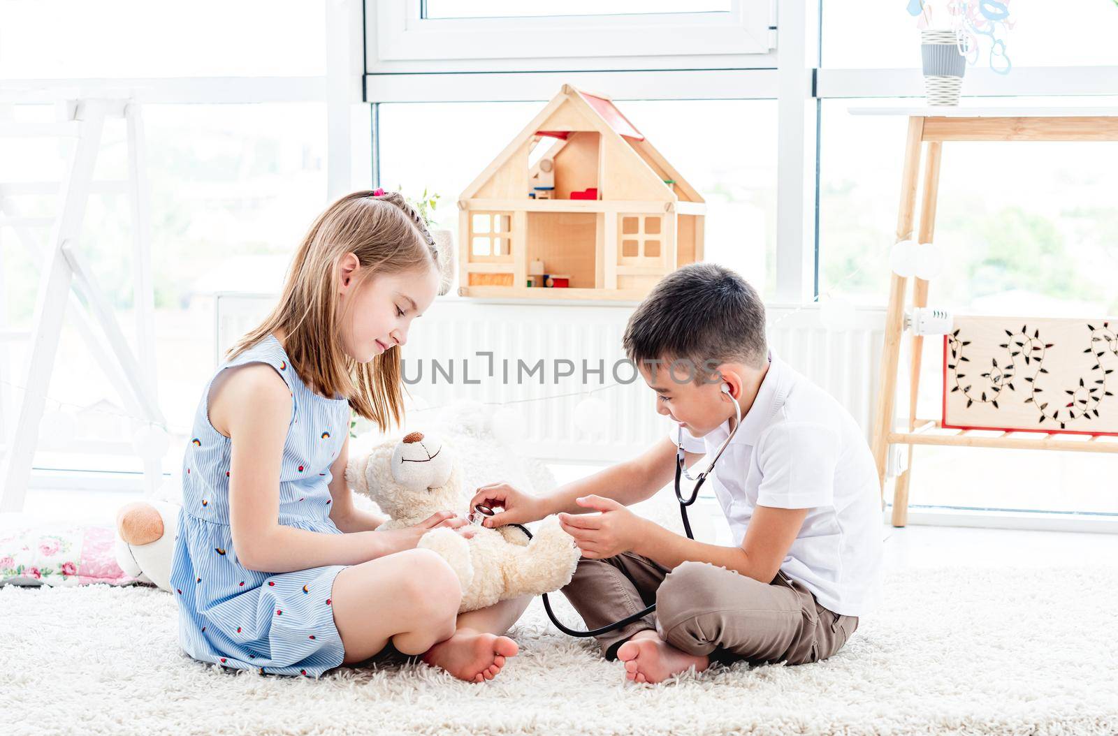 Smiling children playing doctor with teddy bear in bright room