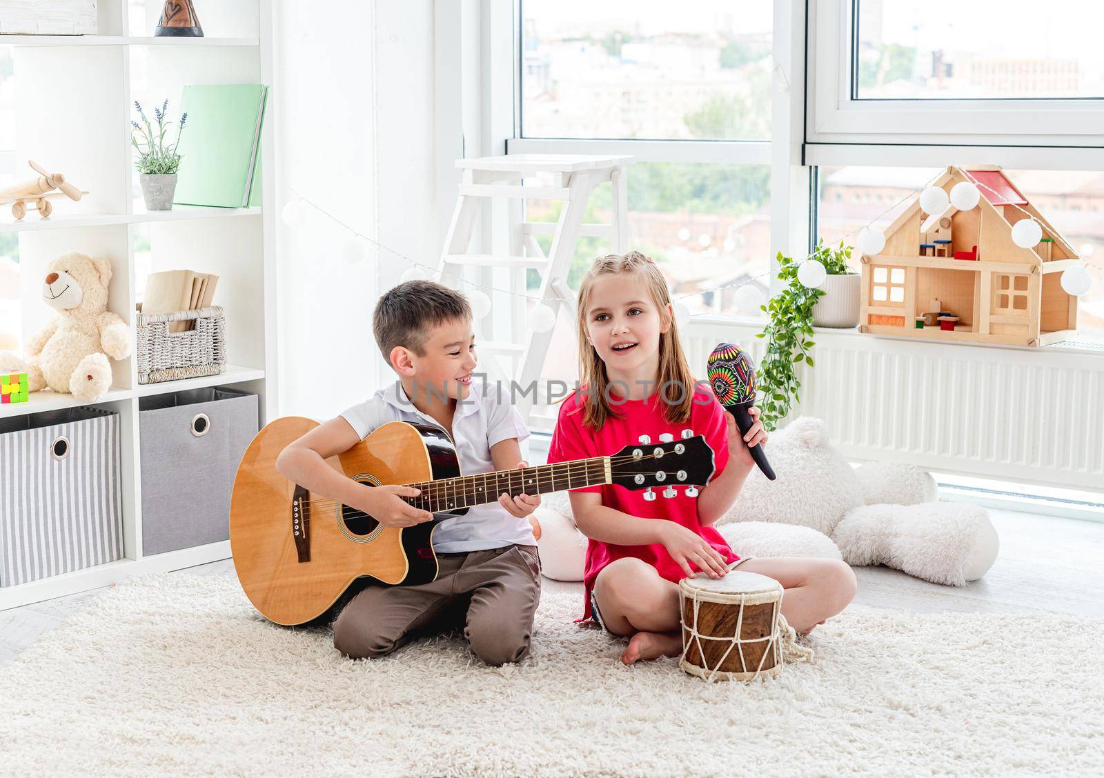 Smiling kids playing on drum and guitar in modern apartment