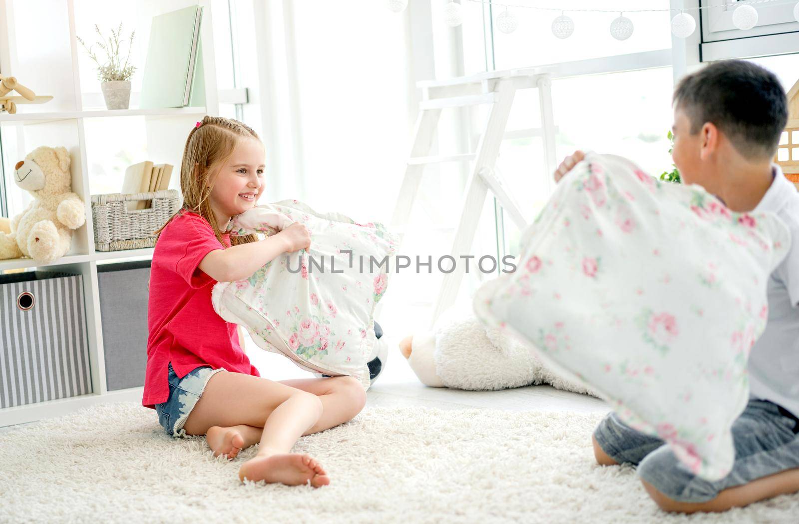 Happy little friends fighting pillows on floor in children's room