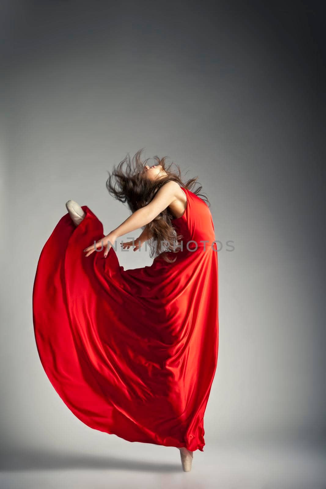 Gorgeous young ballet dancer wearing red dress over dark grey background