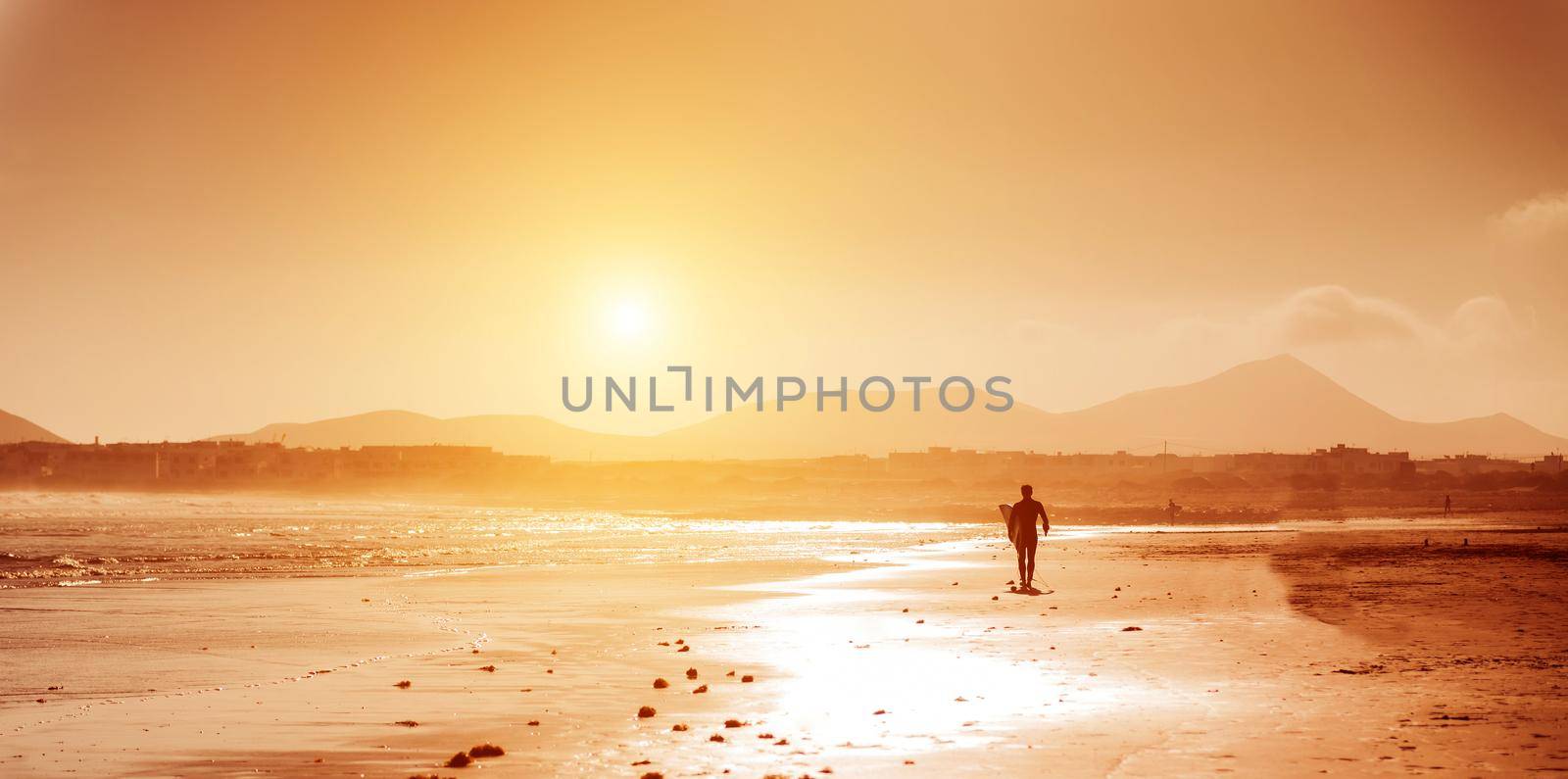 Surfer on the ocean beach at sunset on Canary Islands. Lanzarote, Spain.