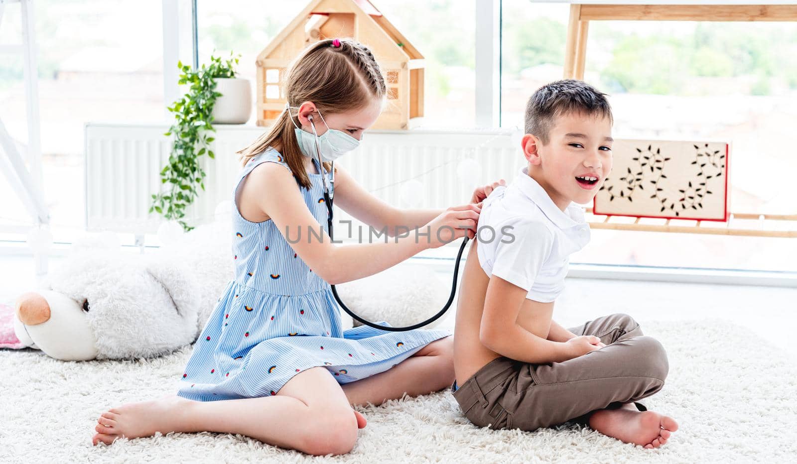 Cute little girl with phonendoscope listening little boy in playroom