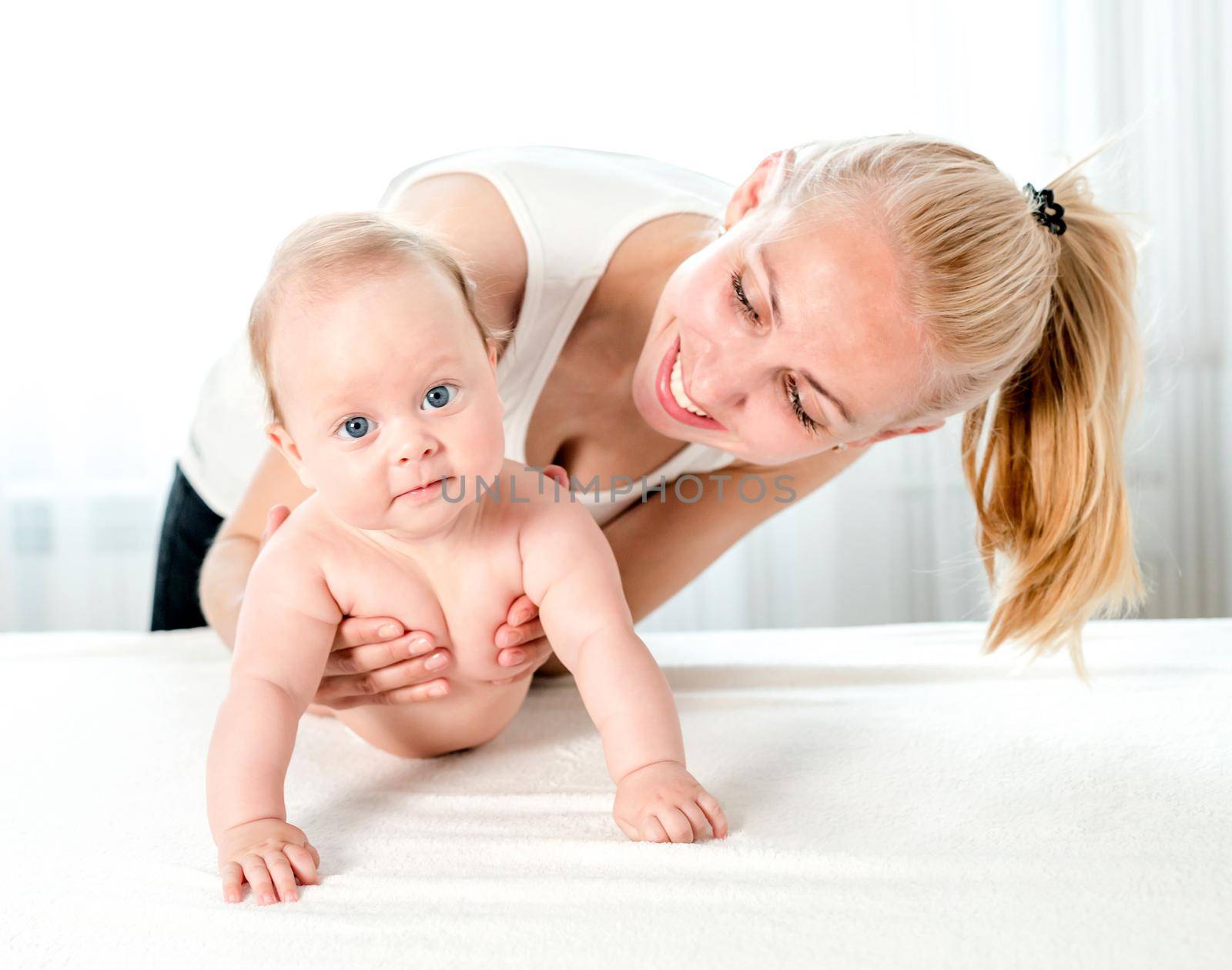 Smiling young mother holding her little newborn baby. Young mother playing with her lovely child at home