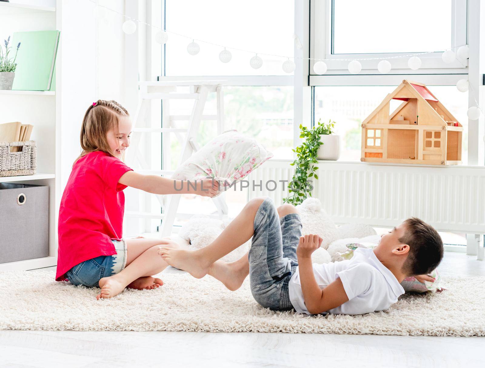 Happy little friends fighting pillows on floor in children's room
