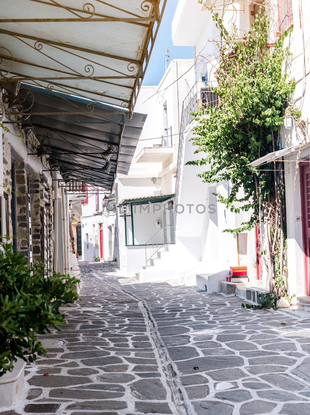 Beautiful narrow street with white houses in Mikonas island, Greece. Traditional narrow street with white facedes of buildings and blue doors