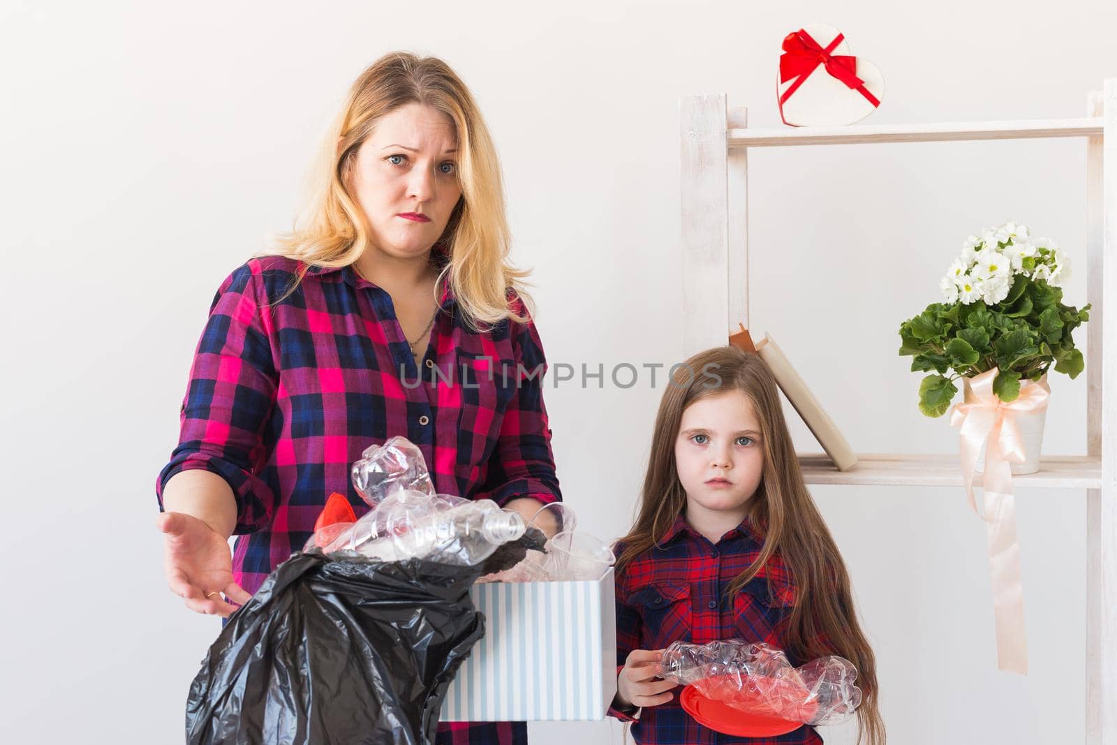 Shocked woman looks with opened eyes and worried expression, holding box with various plastic wastes and trash. by Satura86