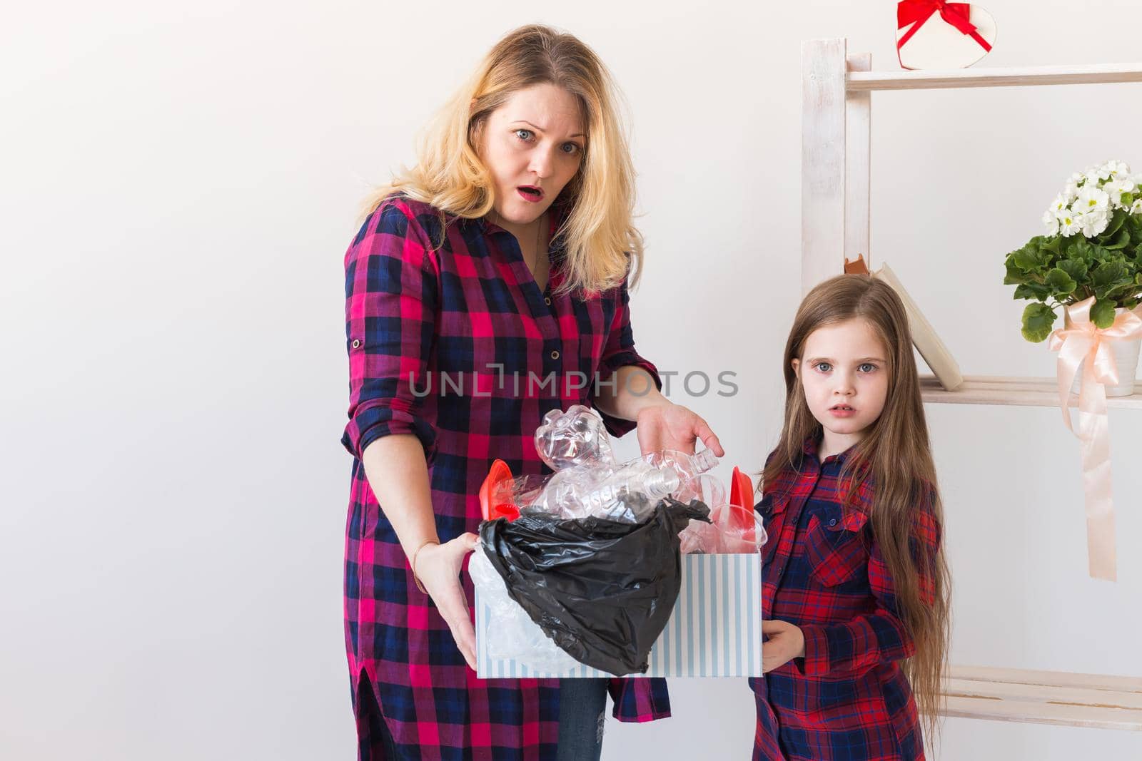 Shocked woman looks with opened eyes and worried expression, holding box with various plastic wastes and trash