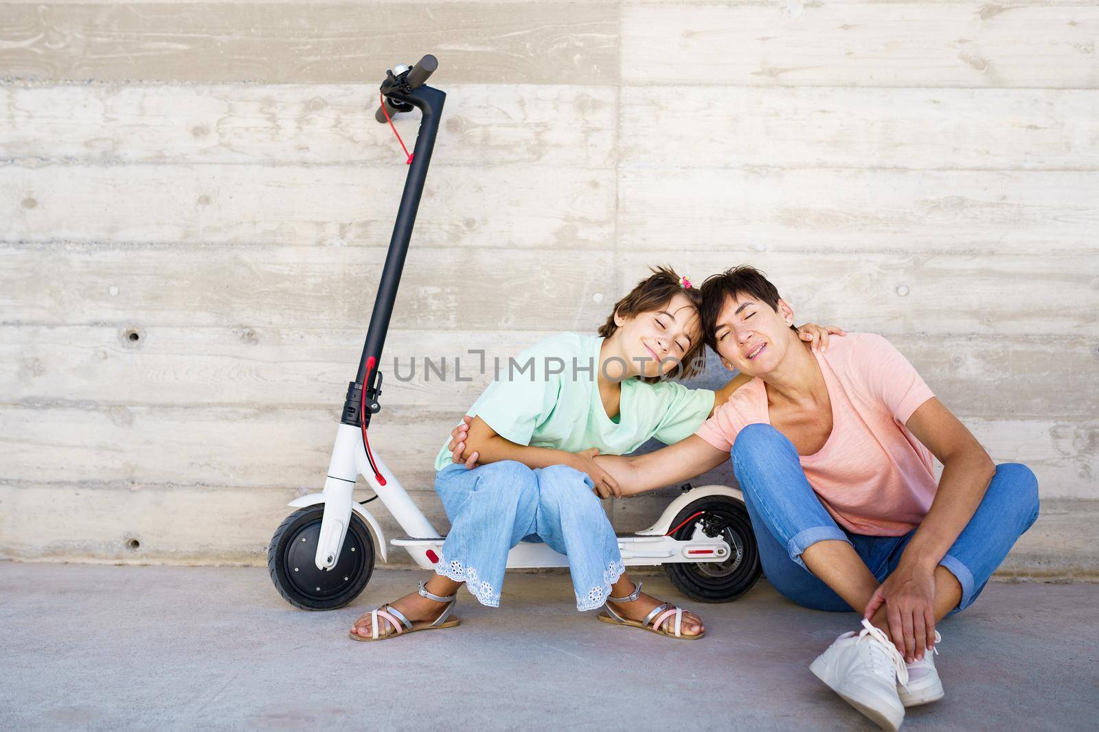 Mother and daughter laughing sitting on an electric scooter in the city street