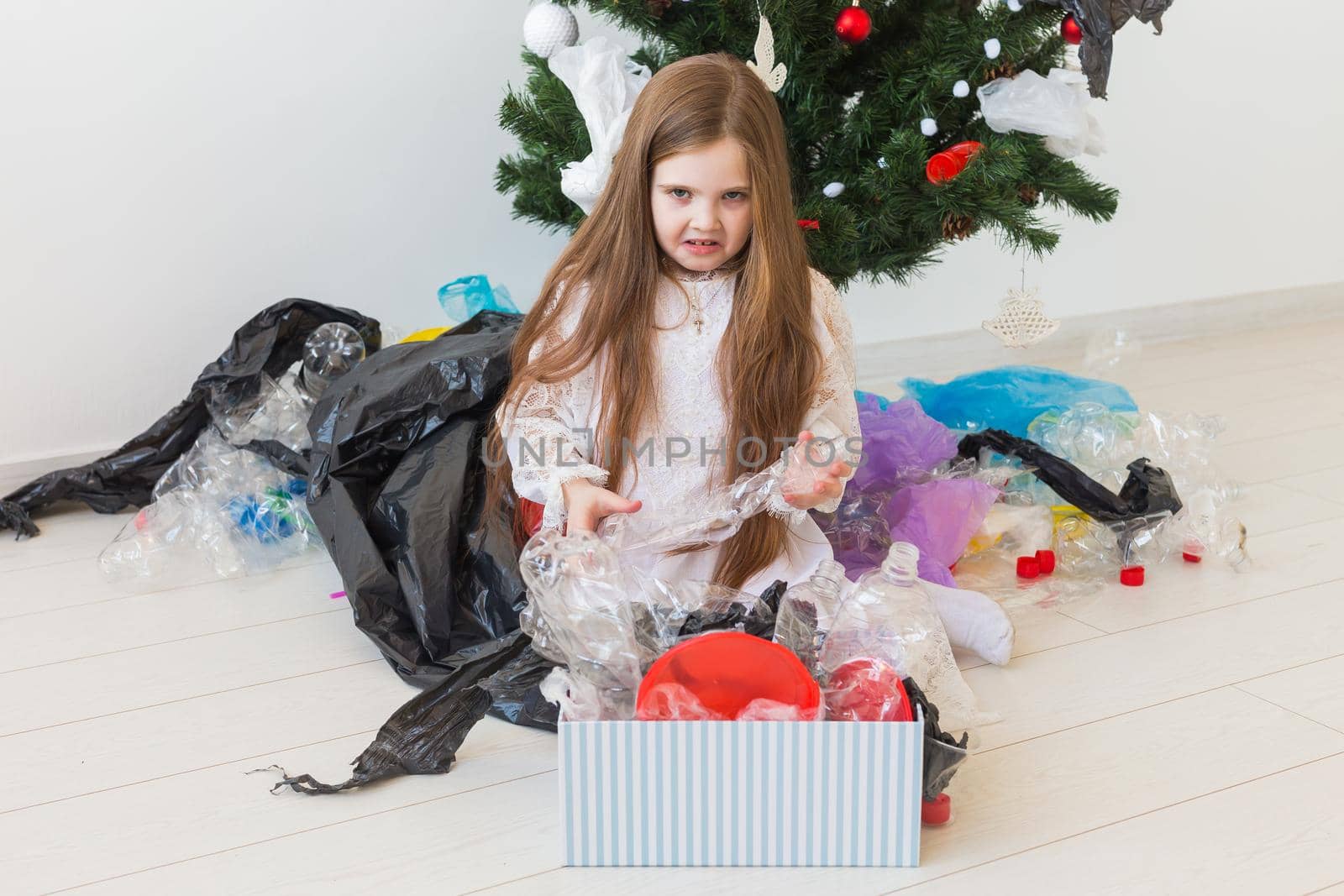 Environmental protection and pollution concept. Sad child carrier box with plastic trash over christmas tree background. by Satura86