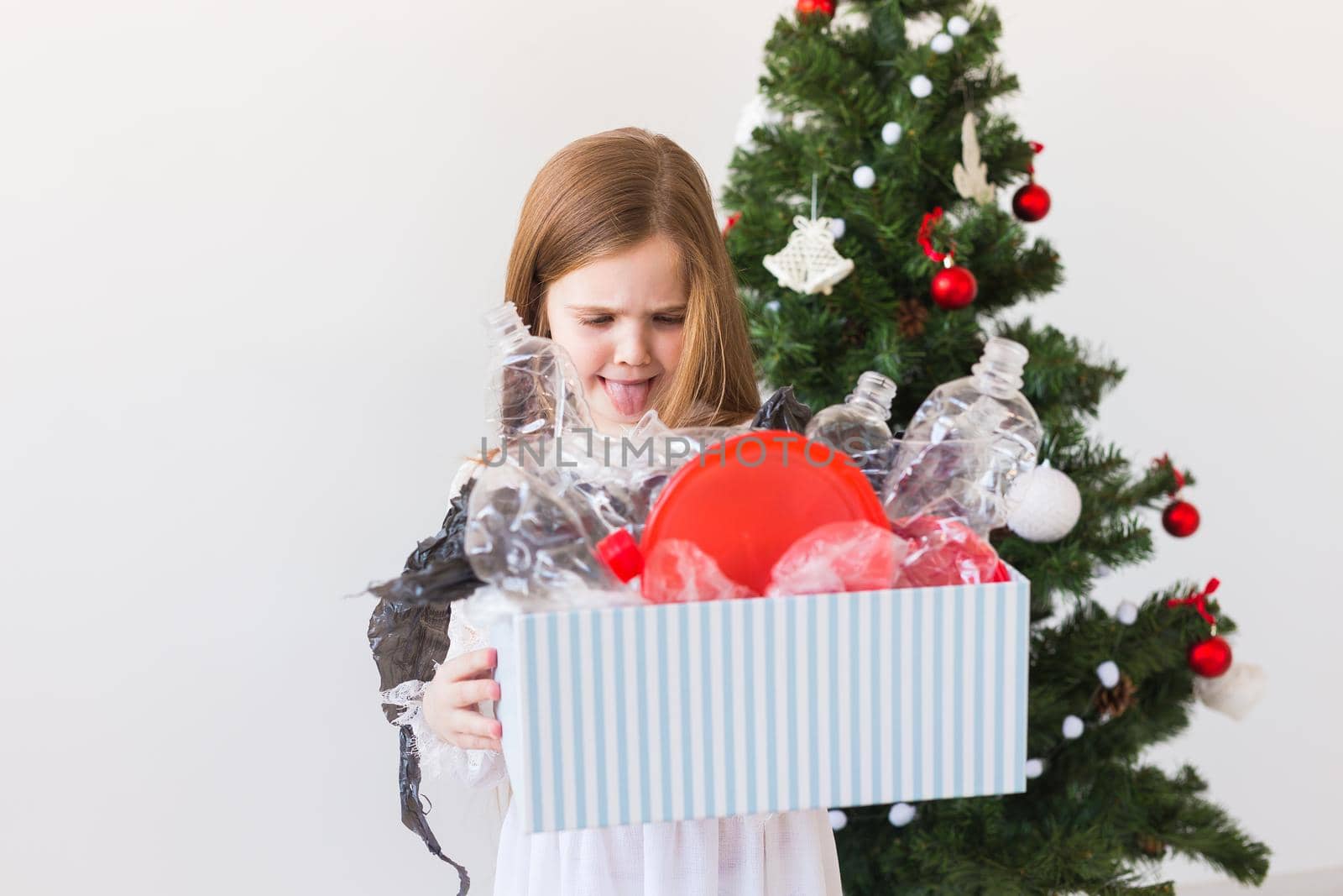 Environmental protection and pollution concept. Surprised child carrier box with plastic trash over christmas tree background