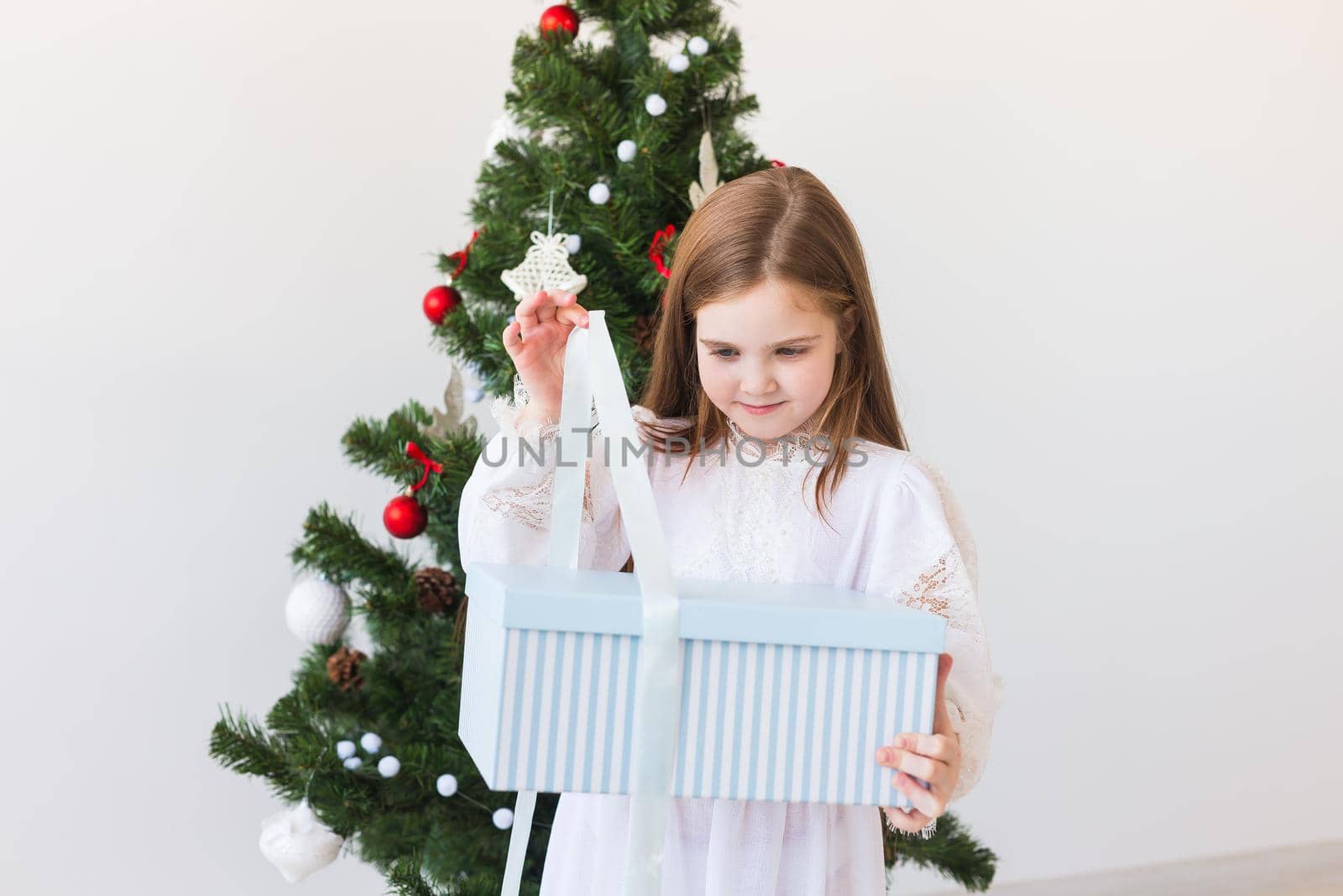Child girl opens gift box near Christmas tree. Holidays, christmas time and presents concept. by Satura86