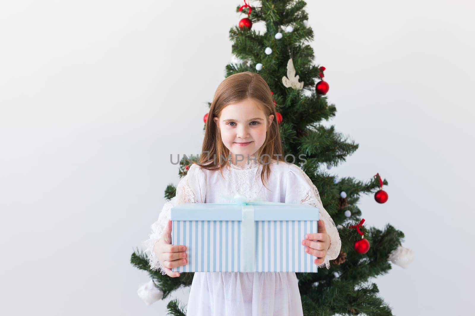 Child girl with gift box near Christmas tree. Holidays, christmas time and presents concept