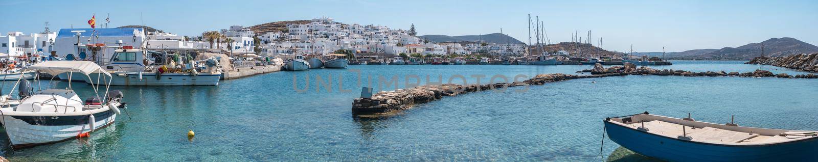 Panorama view of old boats moored in Mykonos harbor and typical white houses on the hill on background
