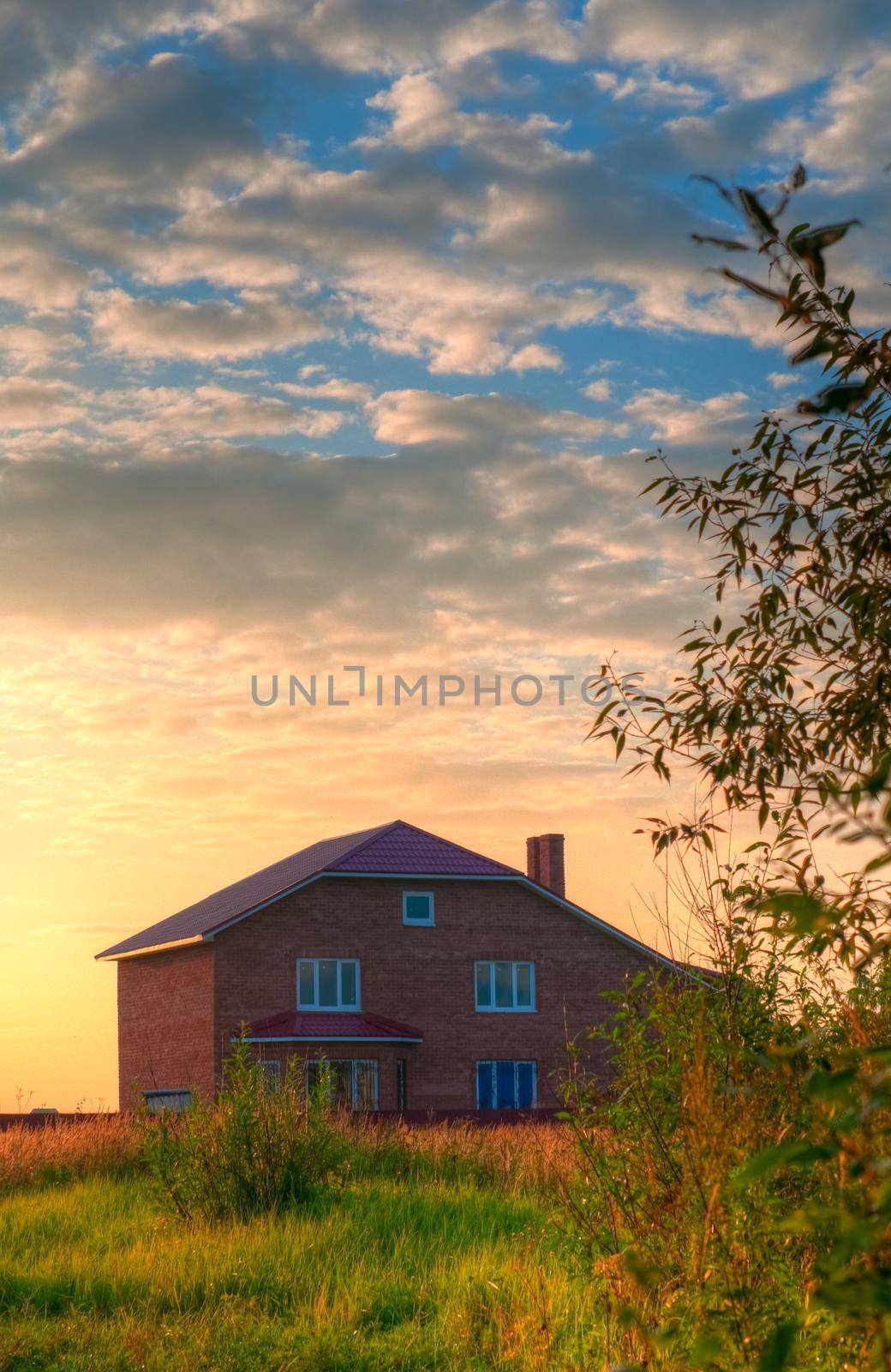 red brick house in the field of yellow flowers with cloudy sky in background
