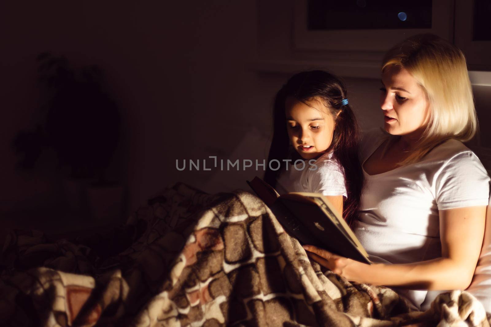 happy family mother and daughter read a book in the evening at home