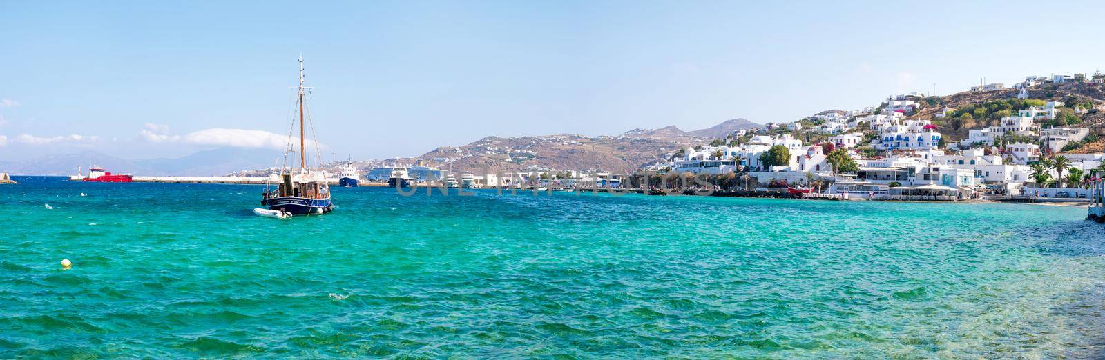 Panoramic view of Greek seaside town with whitewashed houses and floating ships in the water