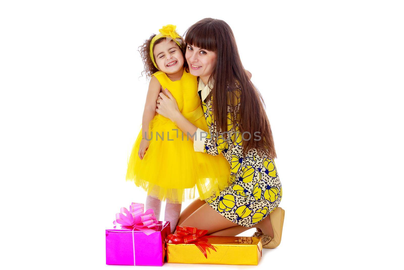 Slender young mother in a short elegant dress and her cute little daughter , embracing, surrounded by Christmas gifts.Isolated on white background.