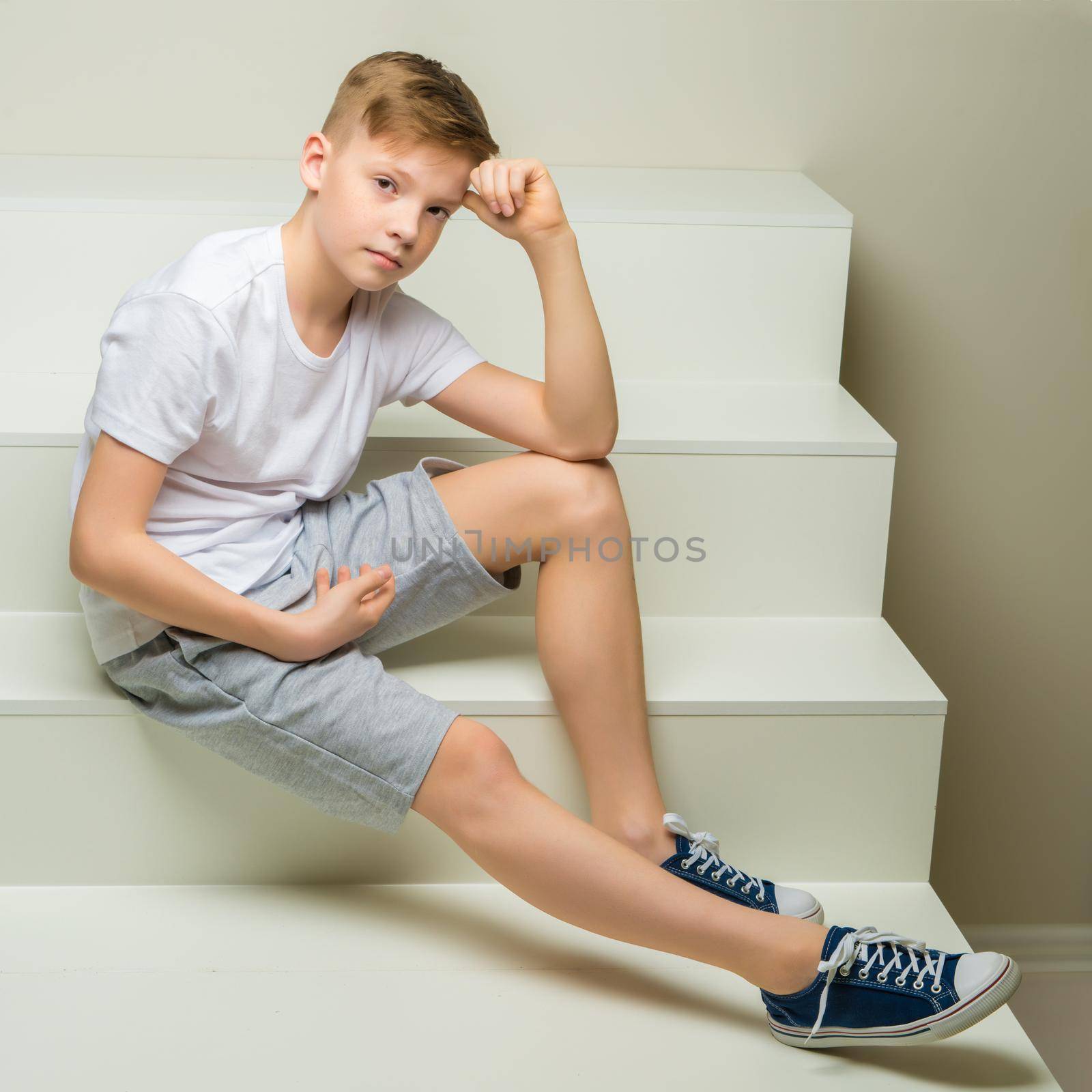 A handsome school-age boy sits on a white staircase. The concept of youth culture.