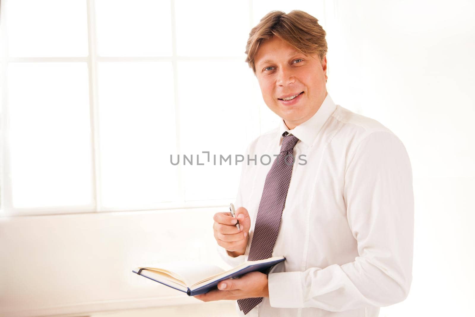 Smiling Businessman in office holding diary by Julenochek