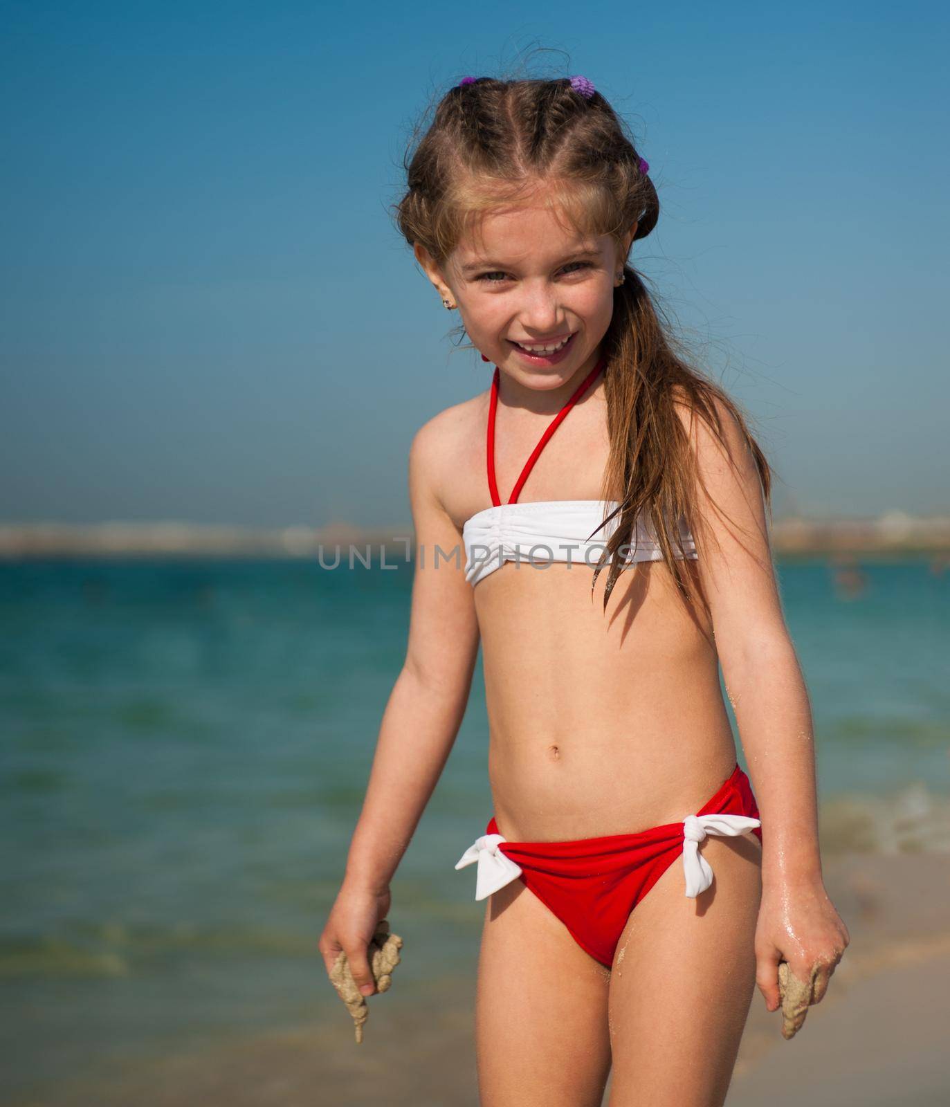 happy cute little girl in red-and-white swimsuit on the beach