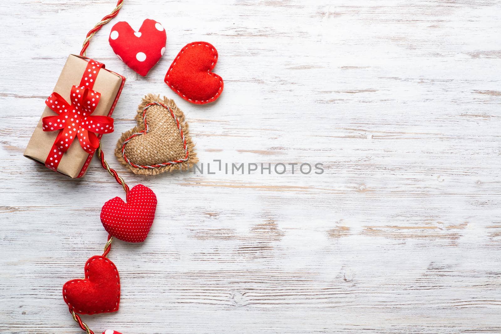 Flat lay cute composition with handmade fabric red hearts. Gift box with ribbon bow on wooden table. Happy birthday or anniversary congratulation. Romantic message template with copy space.