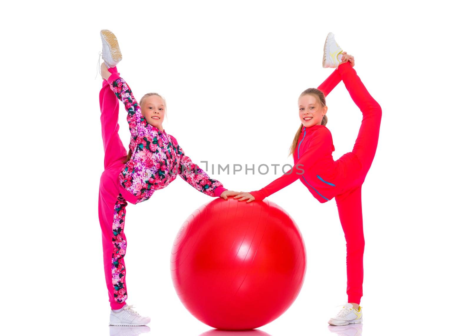 Jolly girls gymnasts perform exercises with a large ball for fitness. The concept of children's sport, a healthy lifestyle. Isolated on white background.
