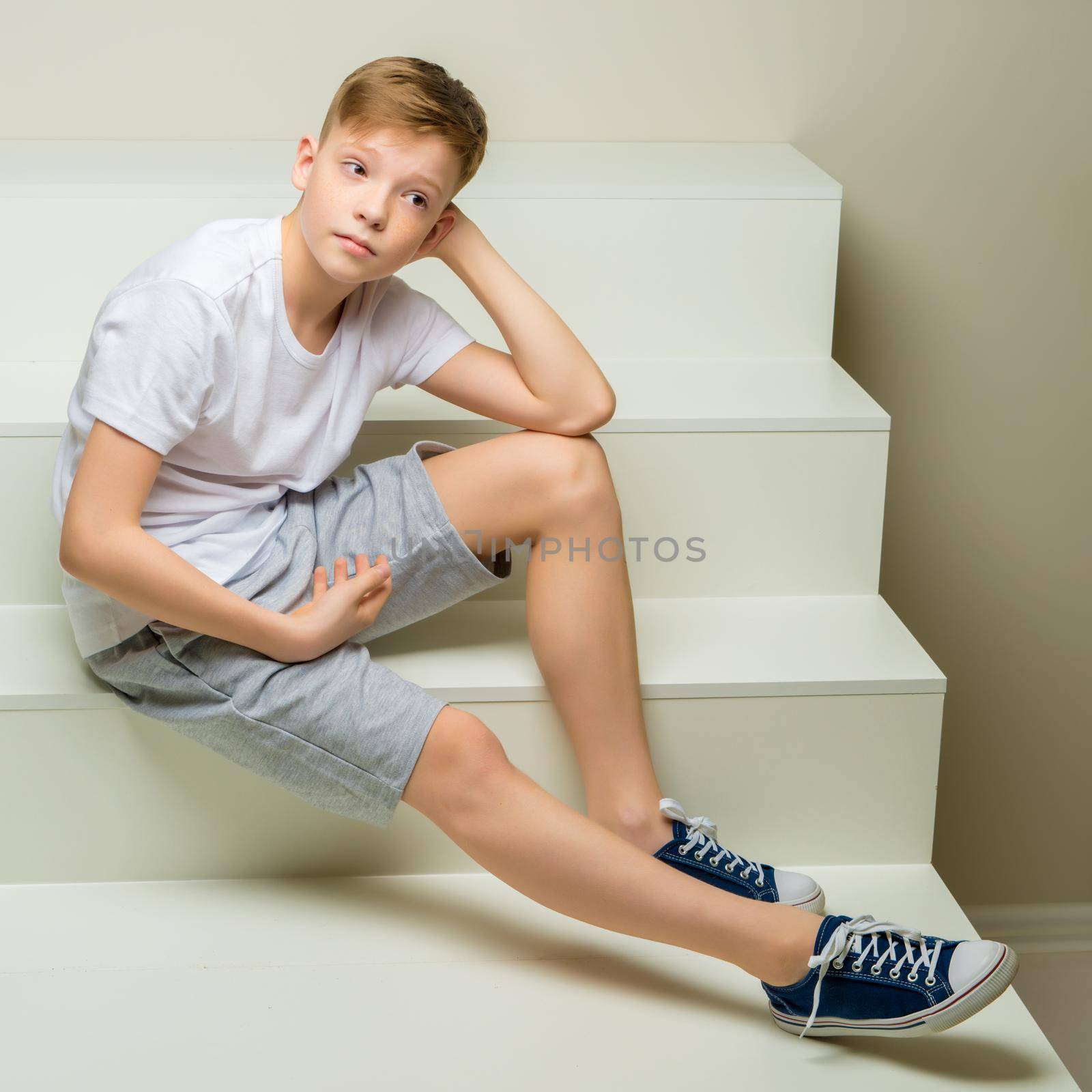 A school-age boy is sitting on a white staircase. by kolesnikov_studio