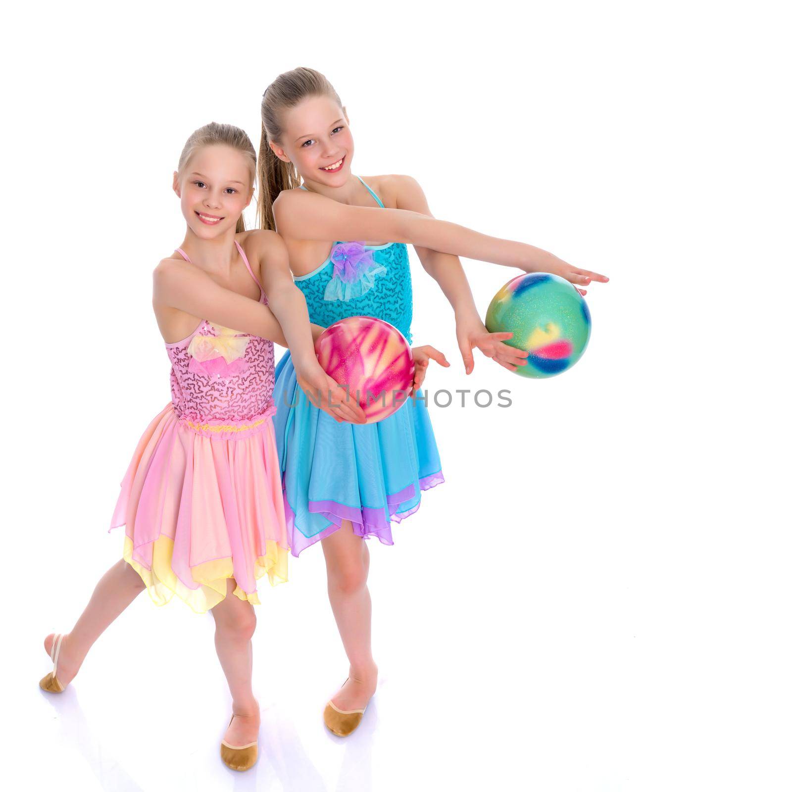 Two cheerful little girls gymnasts in competitions, perform exercises with the ball. The concept of children's sports, fitness, healthy lifestyle. Isolated on white background.