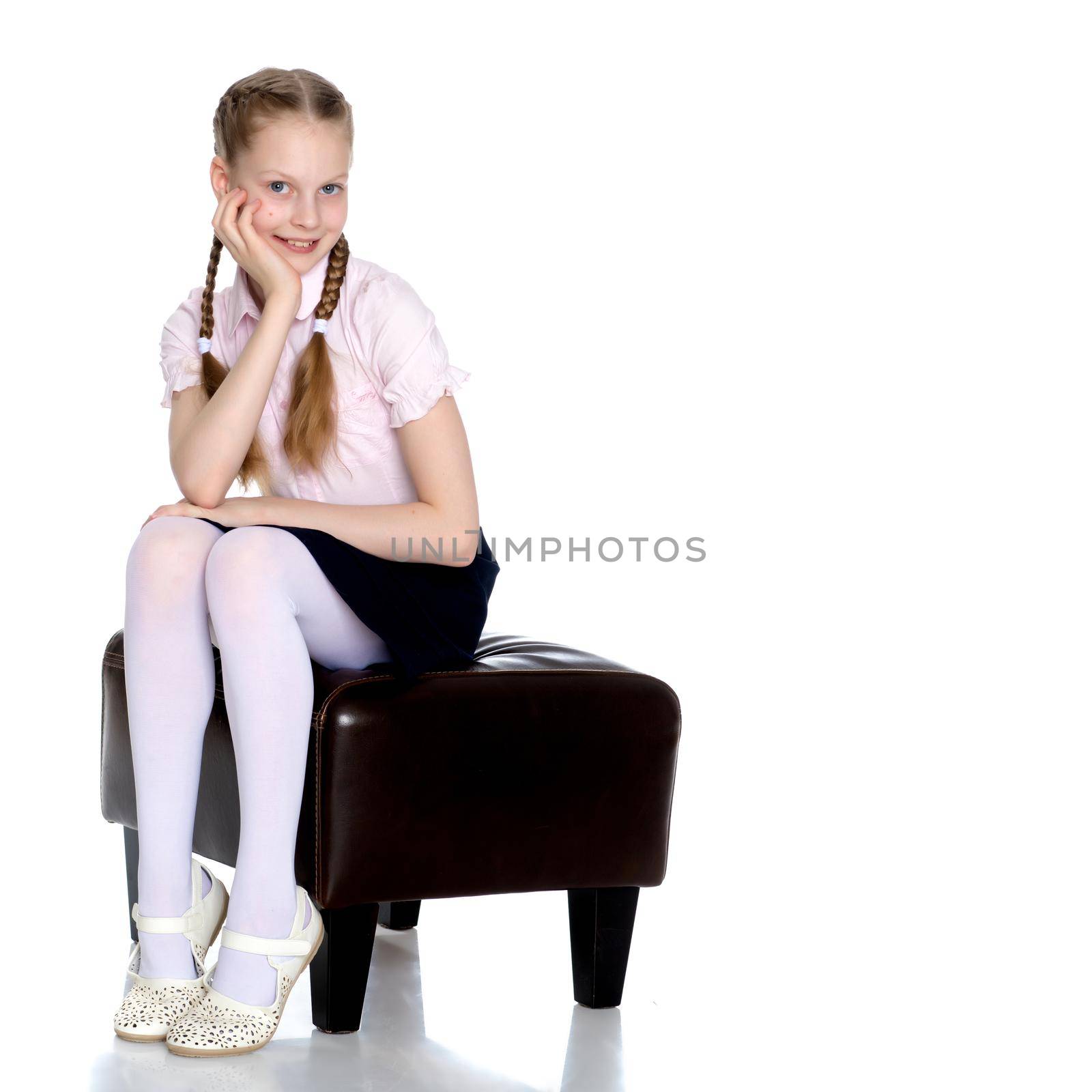 Beautiful schoolgirl girl with long pigtails sitting on the couch. The concept of school fashion, children's emotions. Isolated on white background.